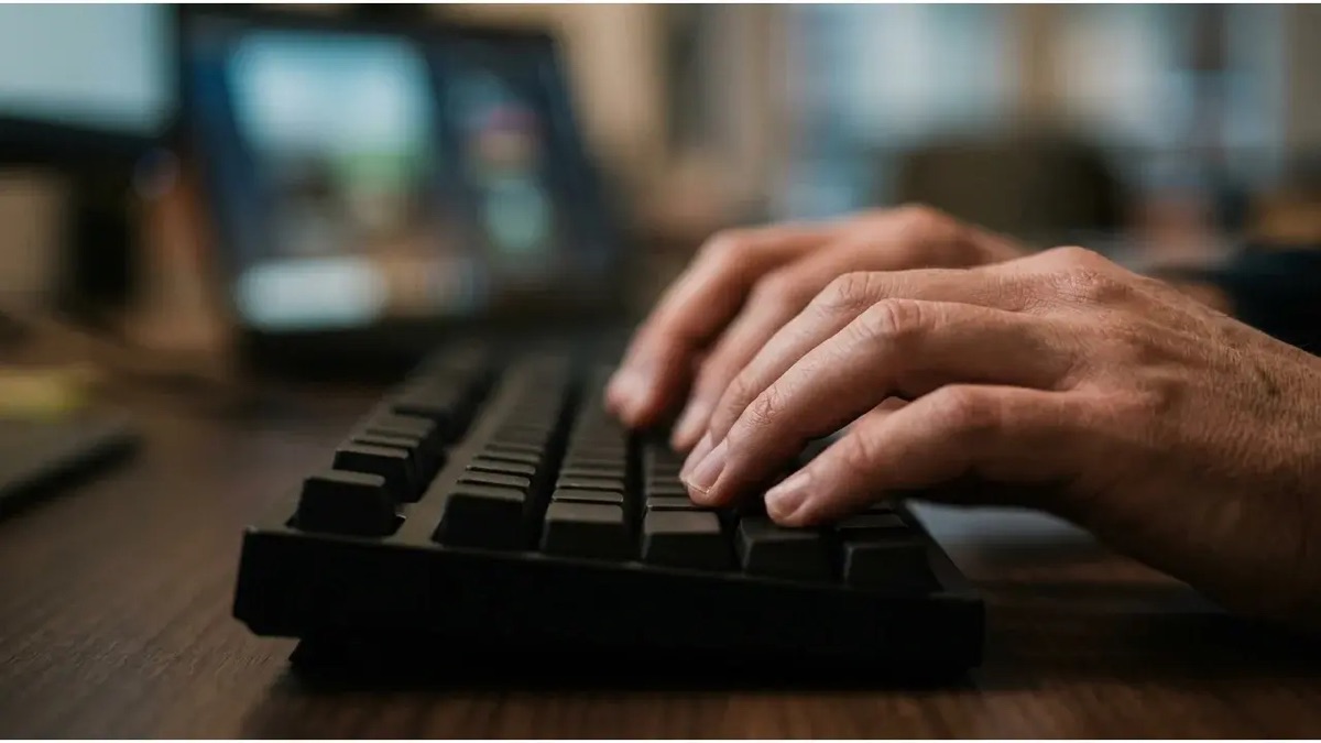 Gros plan sur des mains qui tapent sur un clavier devant un ecran floute